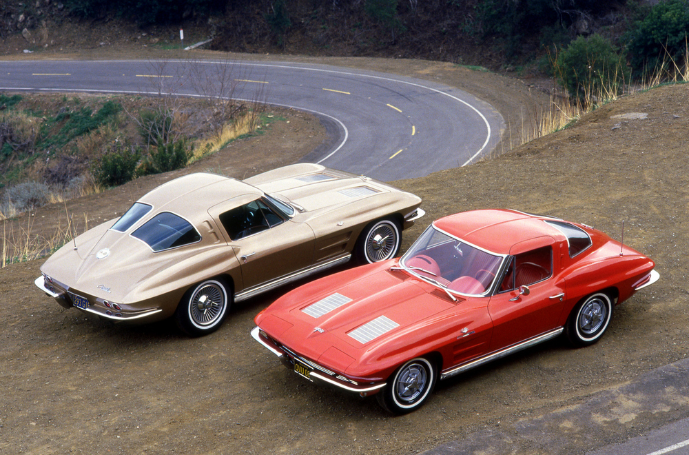 2 Chevrolet Corvette Sting Ray (0800) de 1963, l'une rouge vue de 3/4 avant droit aérienne, l'autre beige vue de 3/4 arrière droit, surplombant un circuit automobile