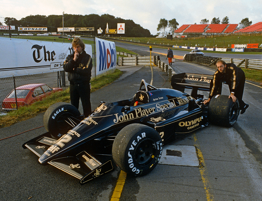 une Lotus 97T 1985 avec un pilote debout à côté et un technicien qui la pousse