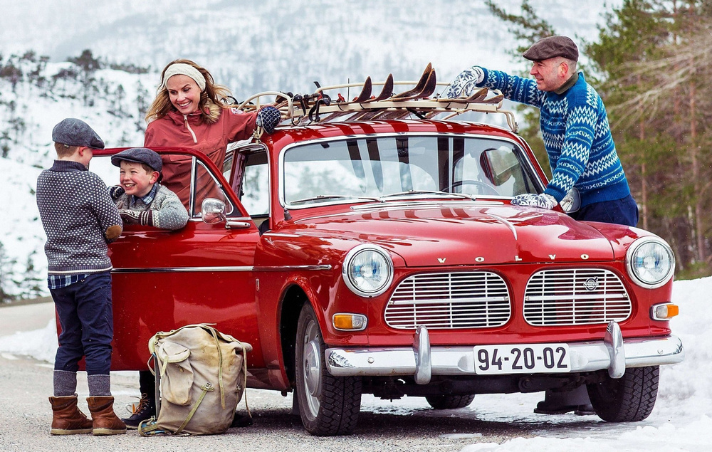 Volvo 122S (P120) 1959–1967 rouge, garée à la montagne dans la neige, avec une famille autour